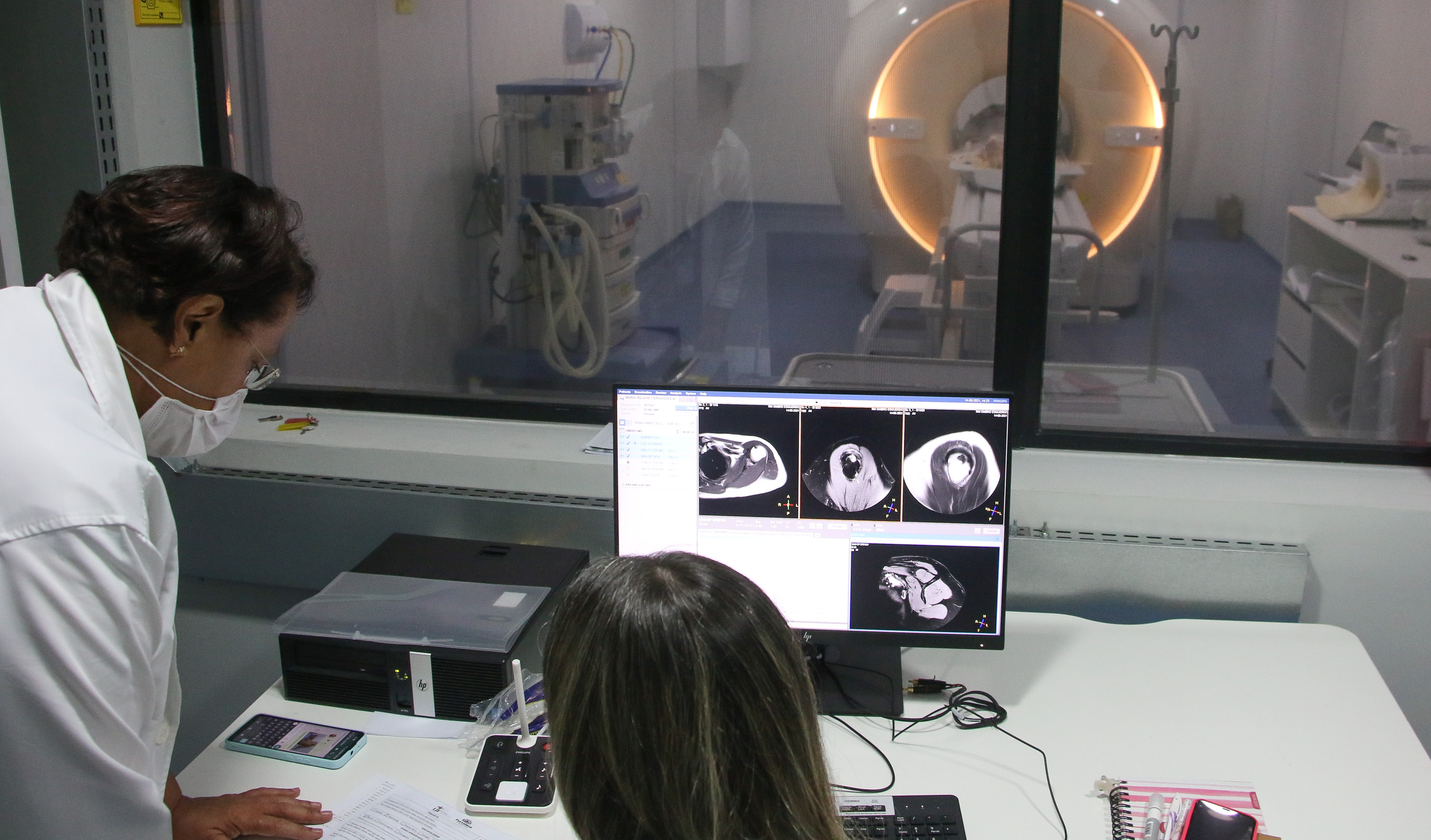 Duas médicas observam a tela de um computador onde aparecem imagens de um exame de ressonângia magnética